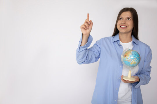 Smiling woman with white teeth holding a globe and showing thumbs up on white background isolate mockup copy space place for text. Tourist trip vacation weekend. Woman traveler in casual clothes 
