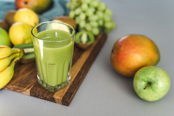 Freshly made a green fruit smoothie and some fruit on the kitchen table.