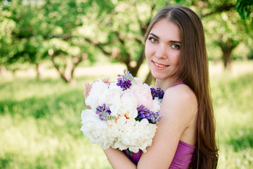 Naklejka premium Pretty gentle young girl in a purple dress in garden with a bouquet in her hands looking at the camera. Professional makeup and dress for bridesmaids in violet. Copy space.