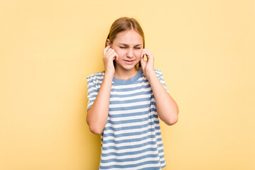 Young caucasian girl isolated on yellow background covering ears with hands.