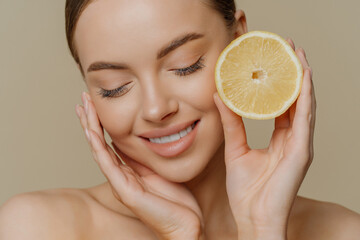 Headshot of sensual charming young woman wears minimal makeup touches face gently holds slice of...