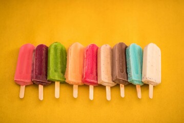 Top view of colorful ice cream bars in row on the yellow background, giving summer vibes