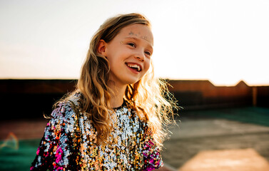portrait of a happy girl in a sequin dress and face paints at sunset