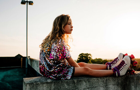girl sat on a wall enjoying the sunset in a dress and roller boots