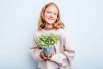 Caucasian teen girl holding a plant isolated on blue background laughing and having fun.