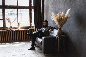 A man with a beard and a smartphone is sitting on a leather sofa.