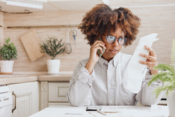 Woman talking on the phone  looking  bills for payment in the kitchen.