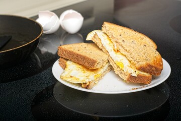 Fried egg sandwich on white plate on stovetop with fry pan and egg shells