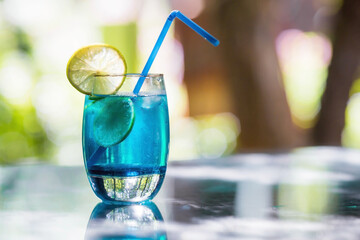 A glass of delicious blue cocktail blue lagoon and yellow lemons on the background of nature. Alcoholic cocktail juicy fruit blue with curacao liqueur, ice cubes and lemon slices.