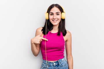 Young caucasian woman listening to music isolated on white background person pointing by hand to a shirt copy space, proud and confident