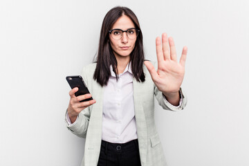 Young business caucasian woman holding mobile phone isolated on white background standing with outstretched hand showing stop sign, preventing you.