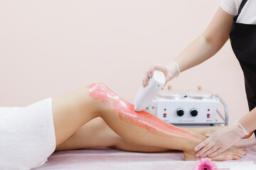 A master applies pink depilatory wax to a young woman's leg for hair removal. Depilation with wax....