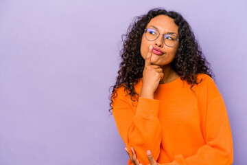 Young hispanic woman isolated on purple background looking sideways with doubtful and skeptical expression. - obrazy, fototapety, plakaty