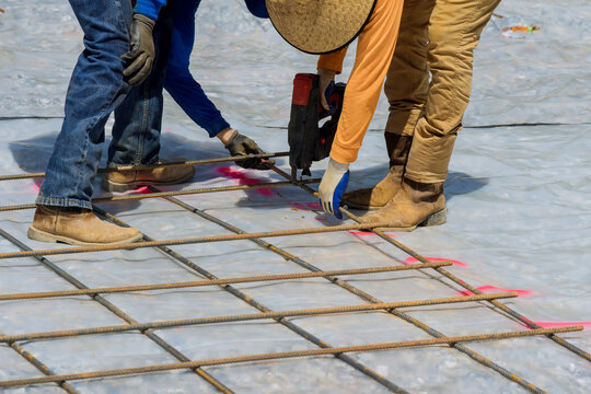 As part of the cement foundation construction process, a construction worker uses rebar tying tool to twist steel bars with wire rod reinforcement.