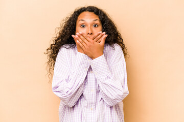 Young hispanic woman isolated on beige background shocked covering mouth with hands.