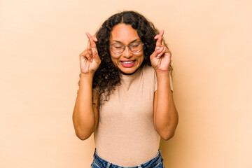 Fototapeta premium Young hispanic woman isolated on beige background crossing fingers for having luck
