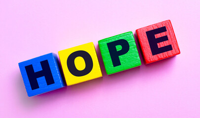 On a light pink background, multi-colored wooden cubes with the text HOPE