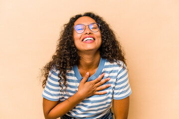 Young hispanic woman isolated on beige background laughs out loudly keeping hand on chest.