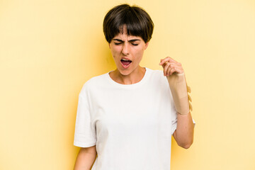 Young caucasian woman hand sling isolated on yellow background screaming very angry and aggressive.