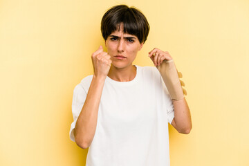 Young caucasian woman hand sling isolated on yellow background showing fist to camera, aggressive...