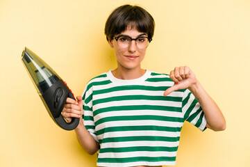 Young caucasian woman holding a hand vacuum cleaner isolated on yellow background showing a dislike gesture, thumbs down. Disagreement concept.