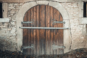 Old medieval arched wooden gate with metal elements and an iron hinge fitting in a stone wall