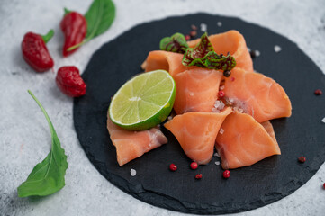 Fresh salmon slices with peppers, greens and lime on concrete background