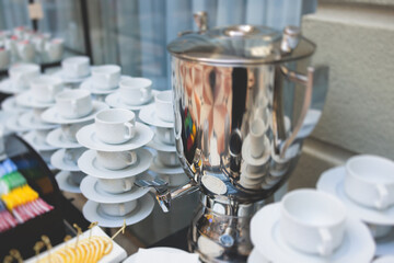 Set of coffee break in the hotel restaurant during conference meeting, with tea and coffee catering, decorated banquet table with white tableware and metal tea maker machine boiler