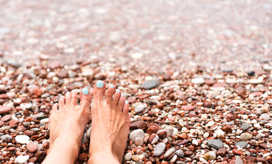 Woman's feet on a pebble beach on the sea. Vacation and travel concept. Rest, relaxation, sunbathing. Close-up. Copy space. Selective focus.