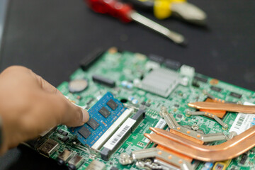 A technician is placing a RAM in a socket of a green computer motherboard at close range.