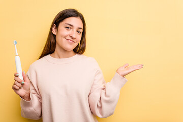 Young caucasian woman holding a electric toothbrush isolated on yellow background showing a copy...