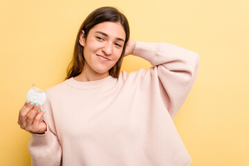 Young caucasian woman holding teeth whitener isolated on yellow background touching back of head, thinking and making a choice.