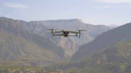 Fototapeta na wymiar Quadcopter flies on background of mountains. Action. View of quadrocopter flying in air on background of mountains. Quadcopter takes pictures of mountain landscapes on sunny day