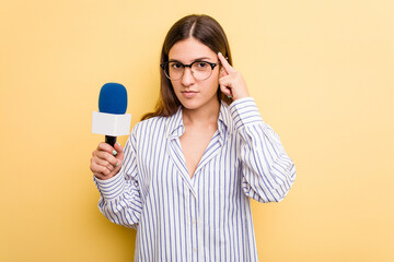 Young caucasian presenter TV woman isolated on yellow background pointing temple with finger, thinking, focused on a task.