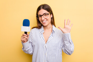 Young caucasian presenter TV woman isolated on yellow background smiling cheerful showing number five with fingers.