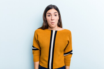 Young caucasian woman isolated on blue background shrugs shoulders and open eyes confused.