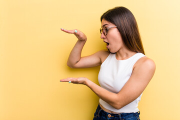 Young caucasian woman isolated on yellow background shocked and amazed holding a copy space between hands.