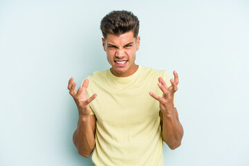 Young caucasian man isolated on blue background upset screaming with tense hands.