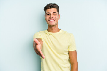 Obraz premium Young caucasian man isolated on blue background stretching hand at camera in greeting gesture.