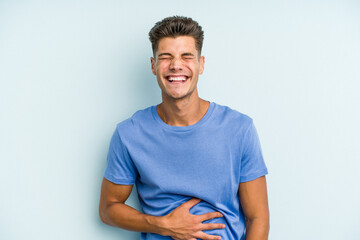 Obraz premium Young caucasian man isolated on blue background touches tummy, smiles gently, eating and satisfaction concept.