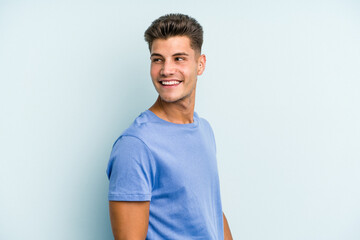 Fototapeta premium Young caucasian man isolated on blue background looks aside smiling, cheerful and pleasant.
