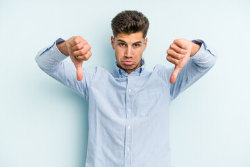 Naklejka premium Young caucasian man isolated on blue background showing a dislike gesture, thumbs down. Disagreement concept.