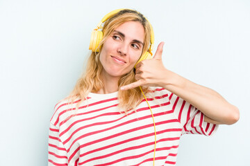 Young caucasian woman listening to music isolated on blue background showing a mobile phone call gesture with fingers.