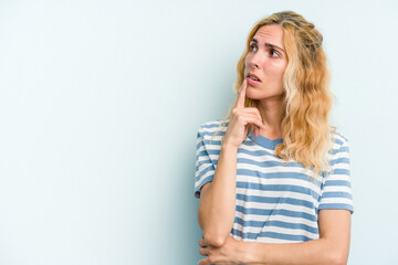 Young caucasian woman isolated on blue background looking sideways with doubtful and skeptical expression.