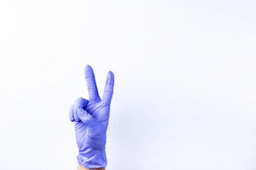 A human hand in a blue medical glove shows a peace sign on a white background.  Lots of empty space