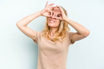 Fototapeta premium Young caucasian woman isolated on blue background showing okay sign over eyes