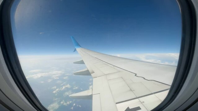 Airplane flying wing view through window illuminator approaching fluffy white cloud clear blue sky
