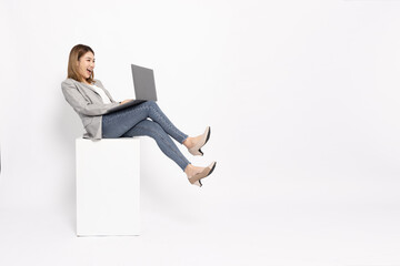 Happy young Asian business woman using laptop computer and sitting on white box isolated on white...