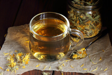 Calendula herbal dried tea in a glass cup with flowers and knitted woollen sweater on wooden rustic...