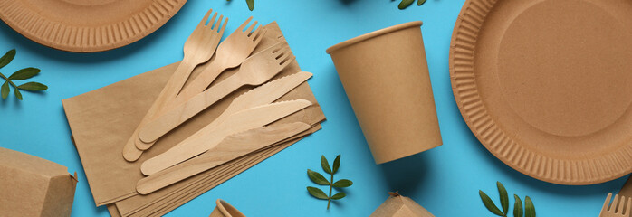 Paper and wooden tableware with green twigs on turquoise background, flat lay. Banner design